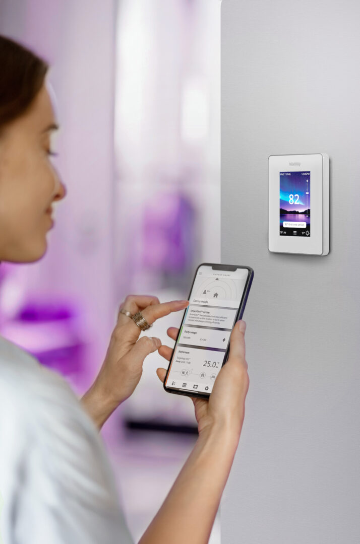A woman using her phone to control Warmup's 7iE Smart Matter Thermostat